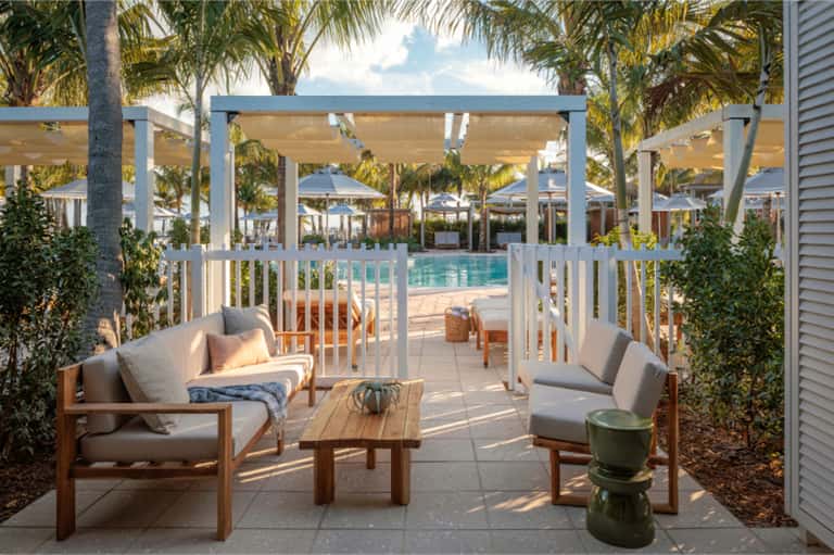 Sunny poolside cabana area with lounge chairs, pergola shade structures, and palm trees
