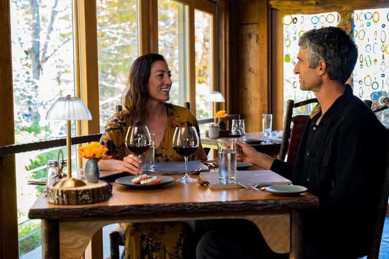 Couple dining at restaurant table with forest view and wine glasses