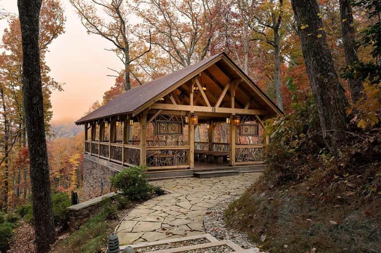 Rustic wooden pavilion with stone patio nestled among autumn trees on hillside at dusk