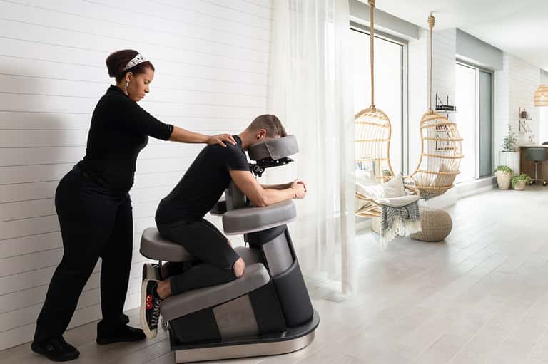 Spa treatment room with massage chair and therapist performing neck massage near hanging wicker chairs