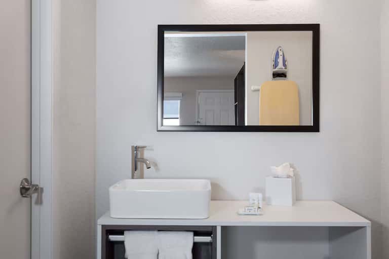 Clean bathroom vanity with white rectangular sink, black-framed mirror, and hotel amenities