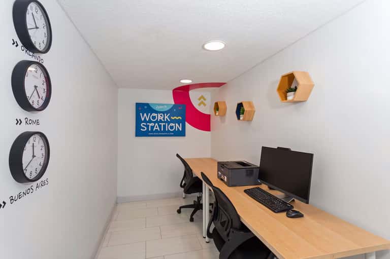 Shared work station with wooden desk, computer setup, world clocks on wall, and hexagonal wooden shelves