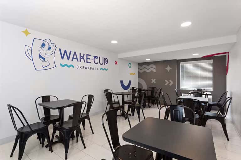 Casual breakfast cafe with cheerful Wake Cup logo, black metal tables and chairs, and geometric wall art