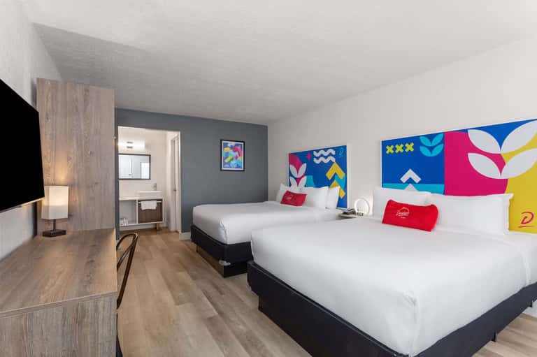 Modern hotel bedroom with two queen beds, colorful abstract headboard art, desk area, and contemporary furnishings