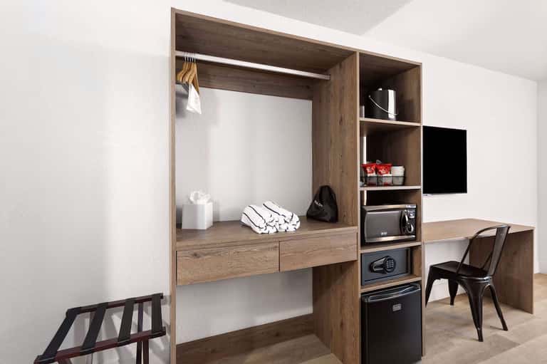 Modern hotel room wardrobe with desk, shelving, TV, and wooden cabinetry