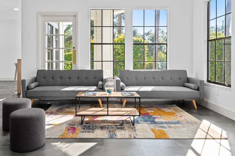 Modern living room with gray sofas, large windows overlooking green landscape, and colorful geometric rug
