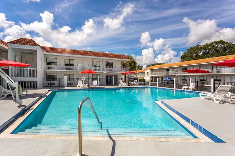 Rectangular swimming pool with metal railings, red umbrellas, and white hotel buildings in background