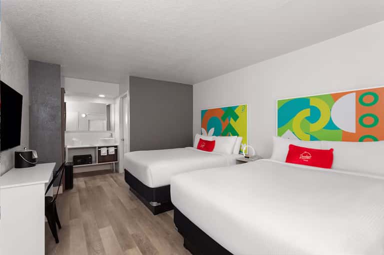Colorful modern hotel room with two queen beds, bright artwork, and ensuite bathroom