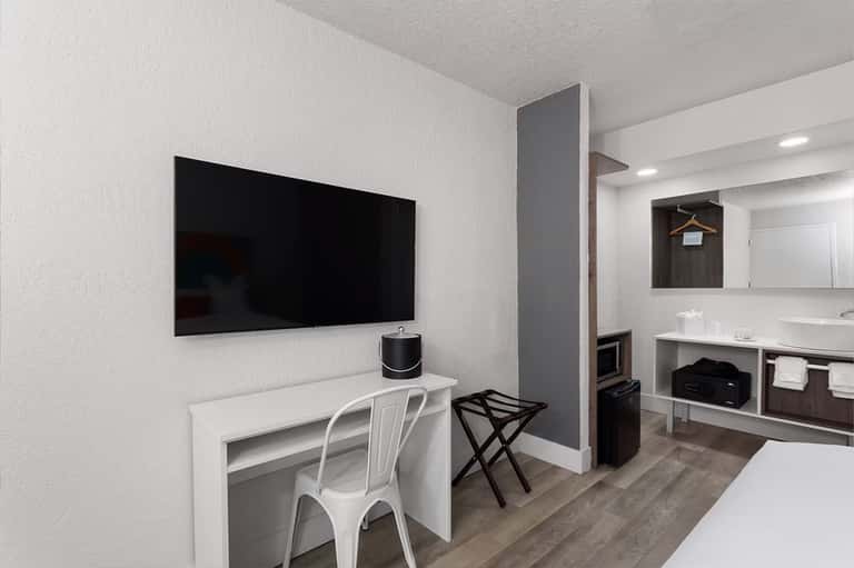 Hotel room workspace with wall-mounted TV, desk, and ensuite bathroom visible
