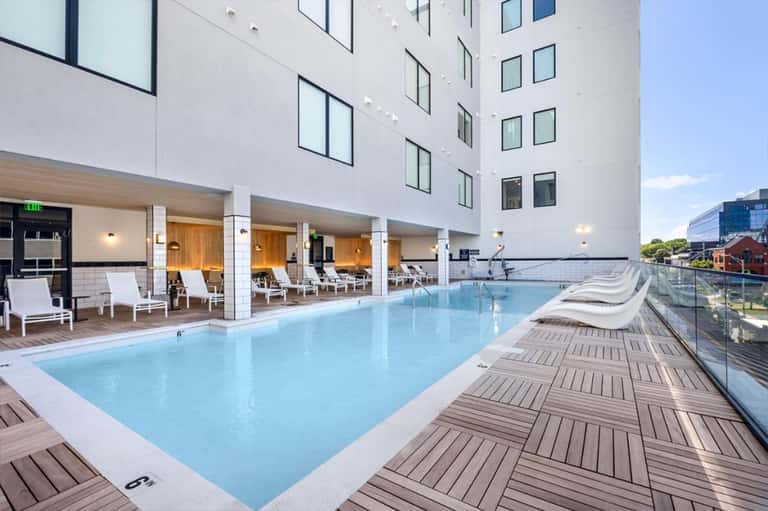 Rooftop swimming pool with lounge chairs, modern building architecture, and water views