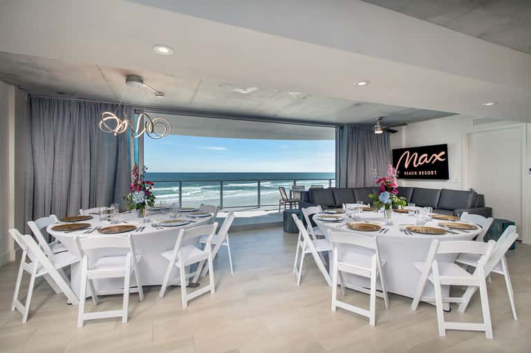 Elegant beachfront event space with banquet tables, ocean views, and floral centerpieces