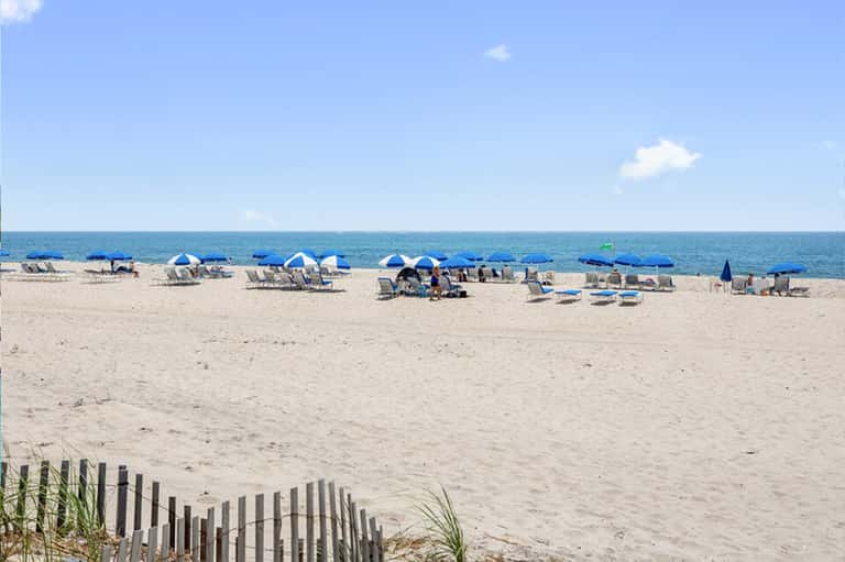 Sandy beach with rows of blue and white umbrellas, beachgoers, and calm ocean water