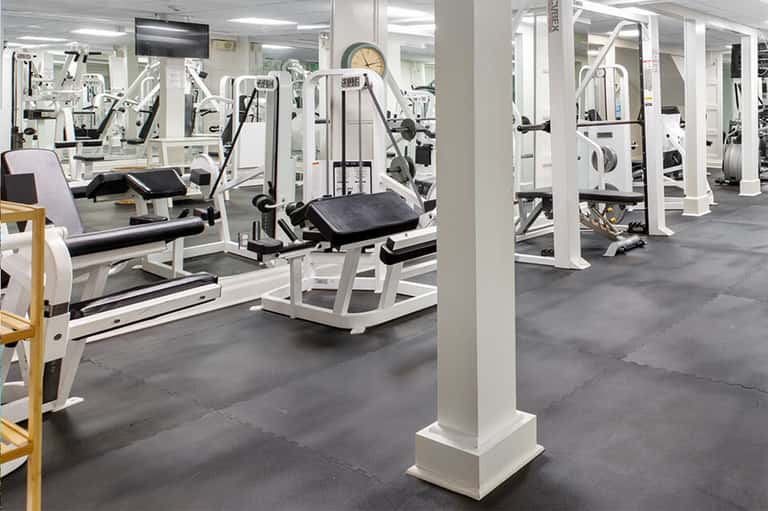 Spacious fitness center with white exercise equipment, machines, mirrors, and bright fluorescent lighting