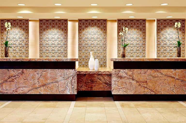 Hotel reception desk with marble countertop, ornate geometric wallpaper, recessed lighting, and fresh flowers