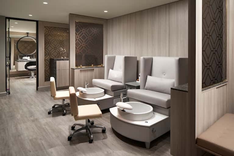 Modern spa pedicure station with white basin chairs, neutral tones, and geometric wall panels