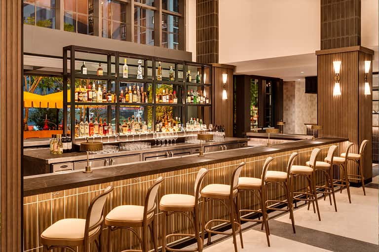 Modern bar with wood paneling, leather bar stools, illuminated shelving, and liquor bottles