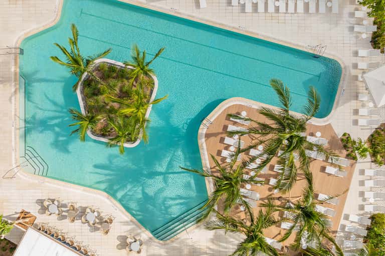 Aerial view of turquoise pool with palm tree islands and wooden deck loungers