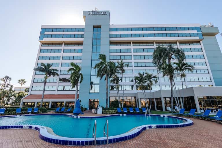 Hilton hotel exterior with curved pool and blue lounge chairs in foreground
