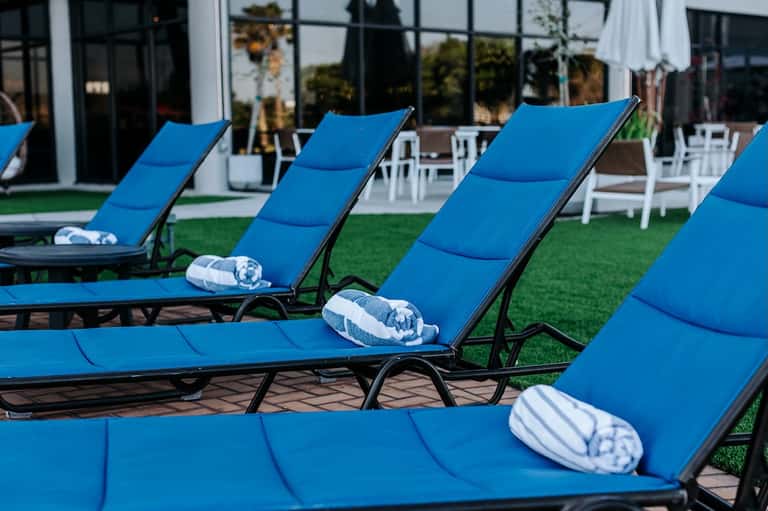 Row of blue chaise lounges with white rolled towels on manicured lawn facing modern building