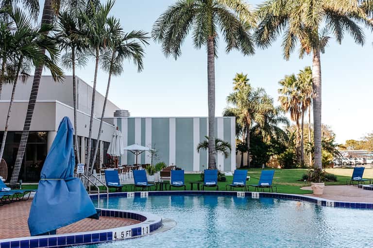 Resort pool with palm trees, blue lounge chairs, and modern building facade