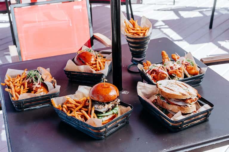 Outdoor dining table with burgers, fried food, and beverages in black serving baskets on patio