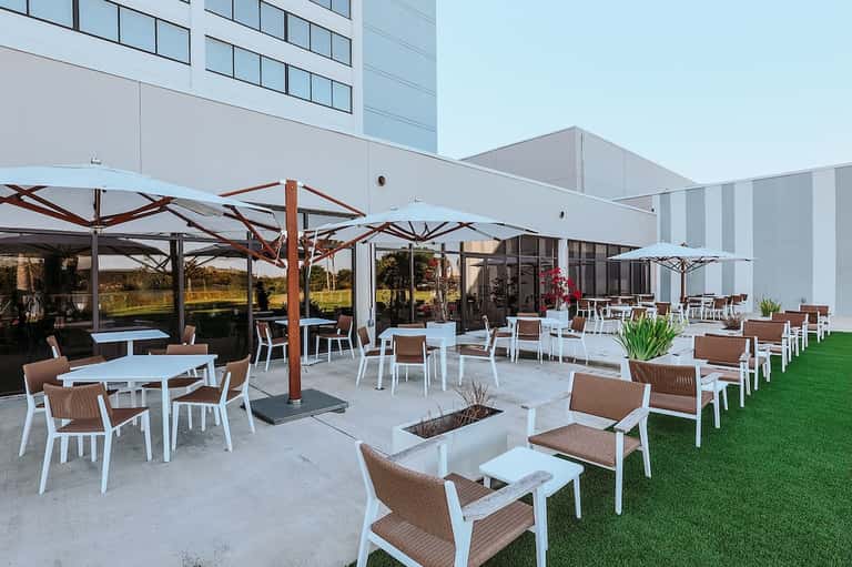Hotel patio with white umbrellas, lounge seating, fire pit, and manicured lawn