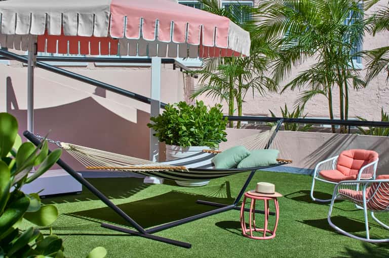 Outdoor deck with hammocks, pink striped awning, potted plants, and wicker chair