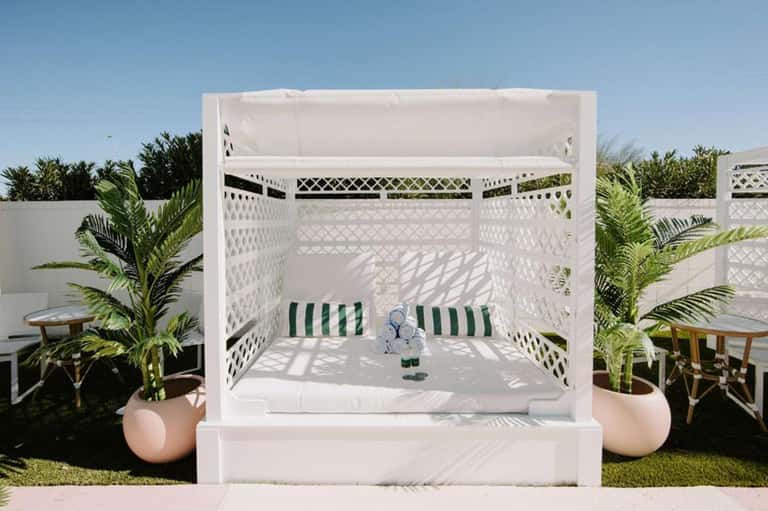 Luxury outdoor canopy bed with white drapes and green striped cushions in tropical garden setting