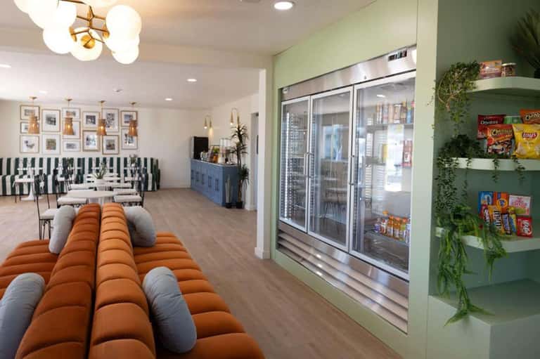 Hotel lobby lounge area with orange puffy seating, striped sofa, green refrigerated beverage displays, and modern lighting
