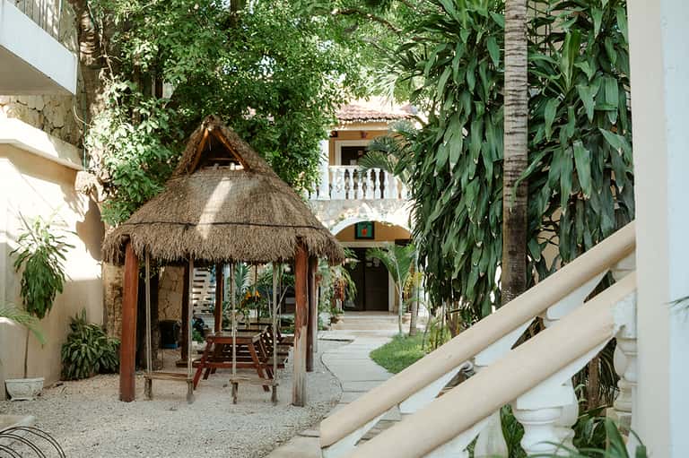 Tropical courtyard with thatched-roof gazebo, colonial architecture, and lush vegetation