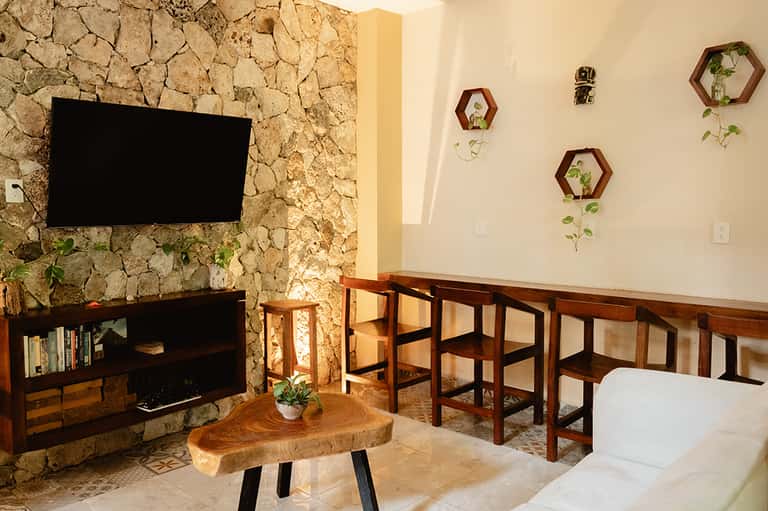Contemporary lounge with stone fireplace, TV, wooden furniture, and hexagonal plant wall decor