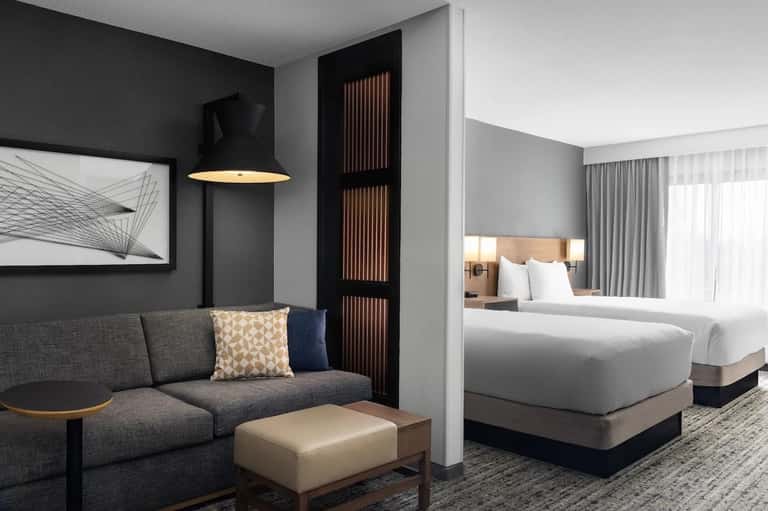 Modern hotel suite with gray sofa, bed visible through partition, and artistic wall decor