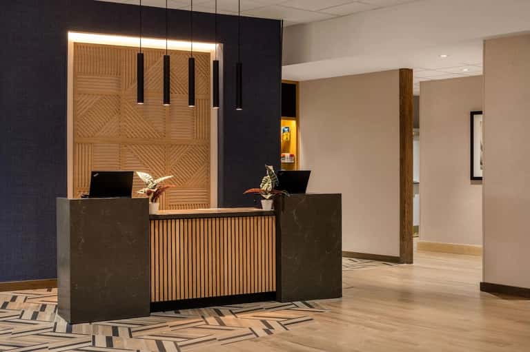 Contemporary hotel lobby featuring wooden accent wall, dark reception desk with pendant lighting