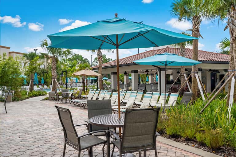 Resort pool deck with turquoise umbrellas, lounge chairs, and palm trees under blue sky