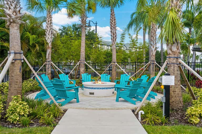 Poolside gathering spot with turquoise Adirondack chairs around fire pit under palm trees
