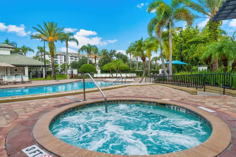 Circular hot tub with palm trees and resort buildings under blue sky