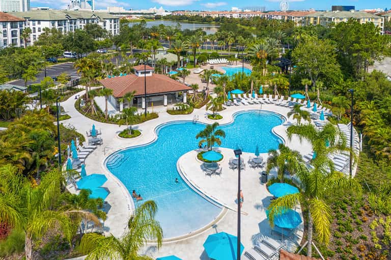 Aerial view of resort with kidney-shaped pool, tropical landscaping, multiple umbrellas, and waterfront location