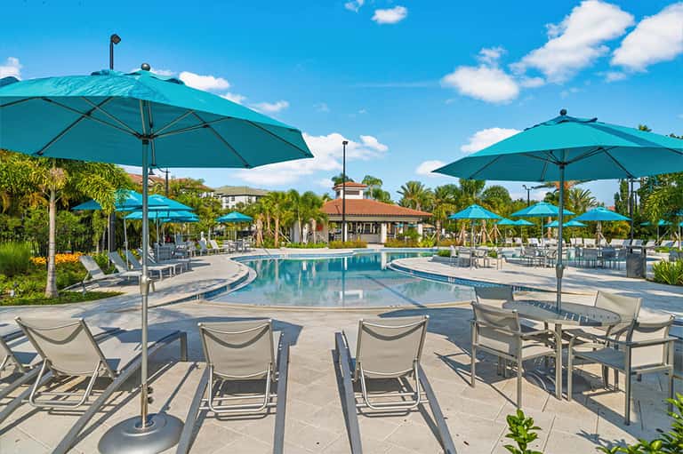 Curved resort pool with turquoise umbrellas, lounge chairs, and thatched-roof structures in background