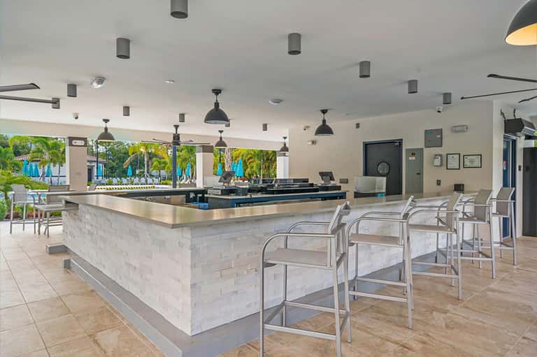Contemporary lobby bar with white brick counter, hanging pendant lights, and pool view
