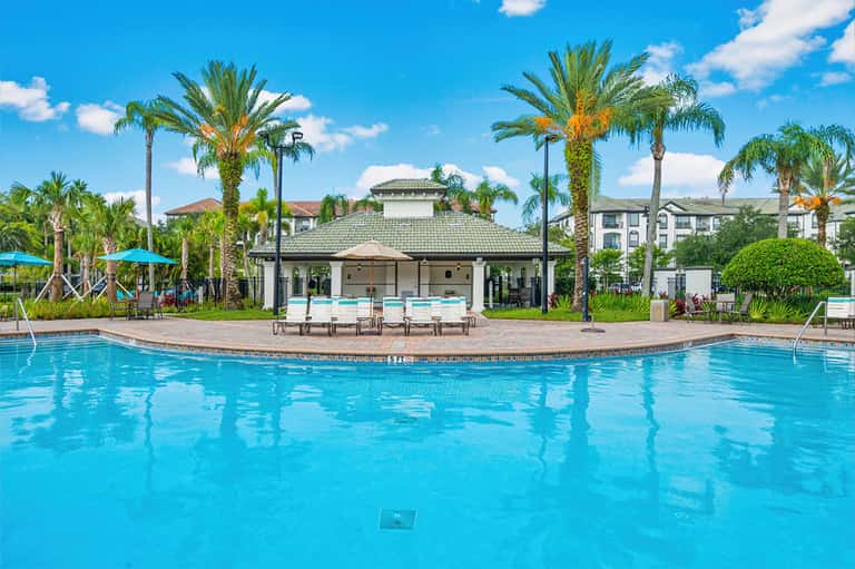 Resort pool with palm trees, cabanas, poolside seating, and residential buildings