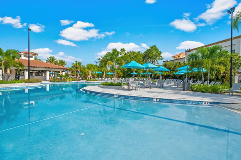 Outdoor pool with blue umbrellas, palm trees, cabanas, and recreational facilities