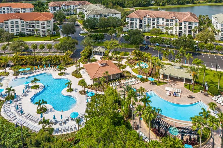 Aerial view of resort complex with multiple pools, palm trees, and residential buildings