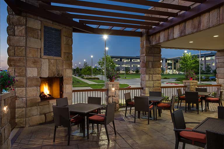 Outdoor patio with fireplace, seating area, and pergola at twilight with green lawn