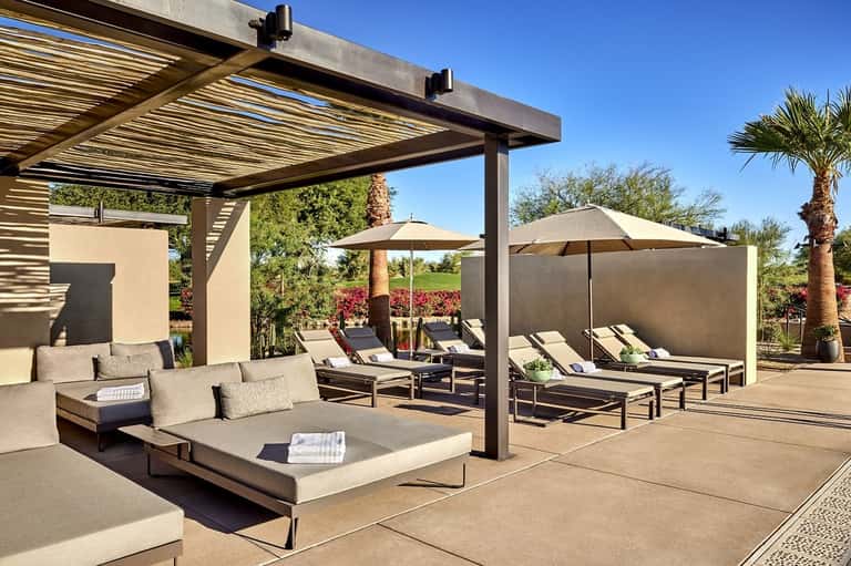 Modern resort patio with lounge seating, pergola shade structure, umbrellas, and manicured grounds