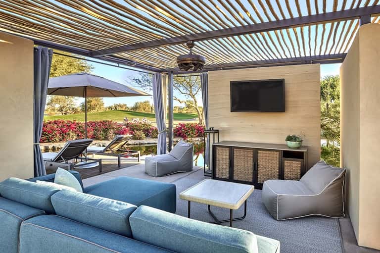 Modern covered patio with lounge seating, flat-screen TV, retractable louvers, and pool views
