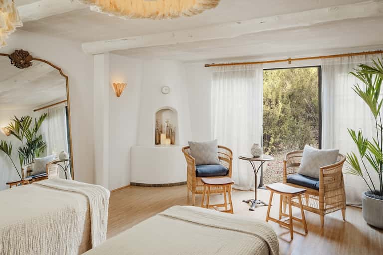 Spa resort room with twin beds, wicker chairs, and glass doors overlooking nature