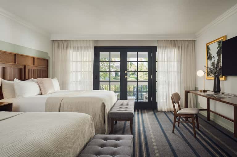 Hotel room with two queen beds, dark balcony doors, curtains, and mid-century modern furnishings