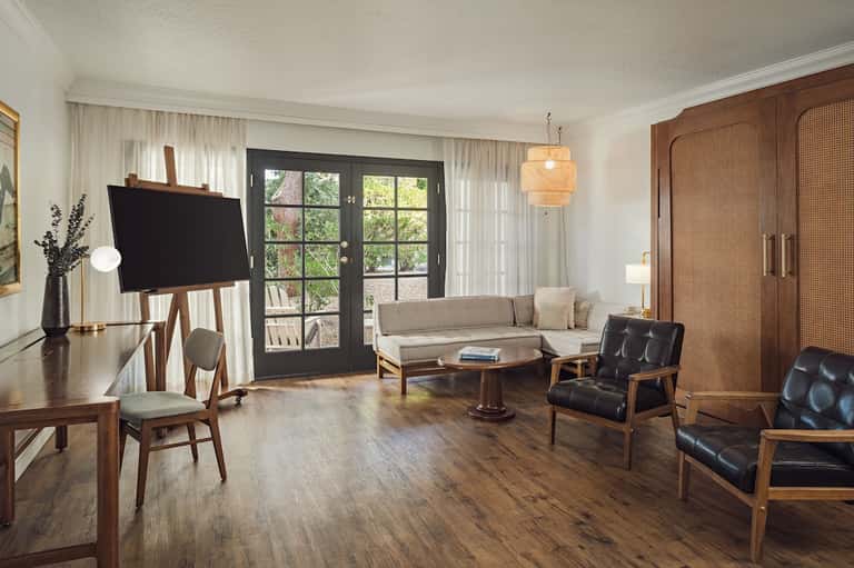 Modern hotel suite living room with wood furniture, TV, neutral sofa, and French doors to patio