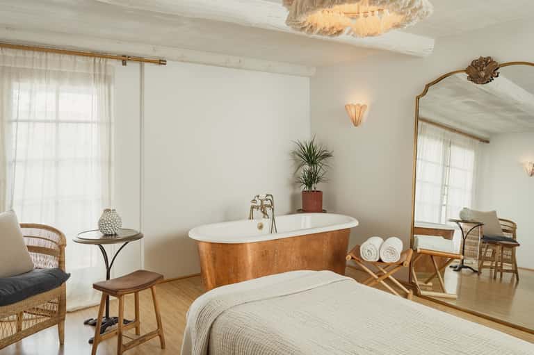 Luxury spa bathroom with copper soaking tub, natural wood furniture, and floor-to-ceiling windows with sheer curtains