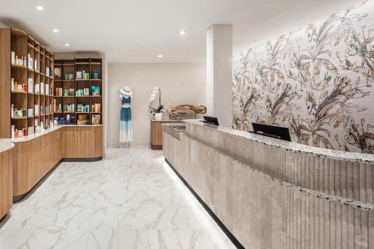 Elegant spa reception area with marble floors, wood cabinetry, botanical wallpaper, and soft lighting